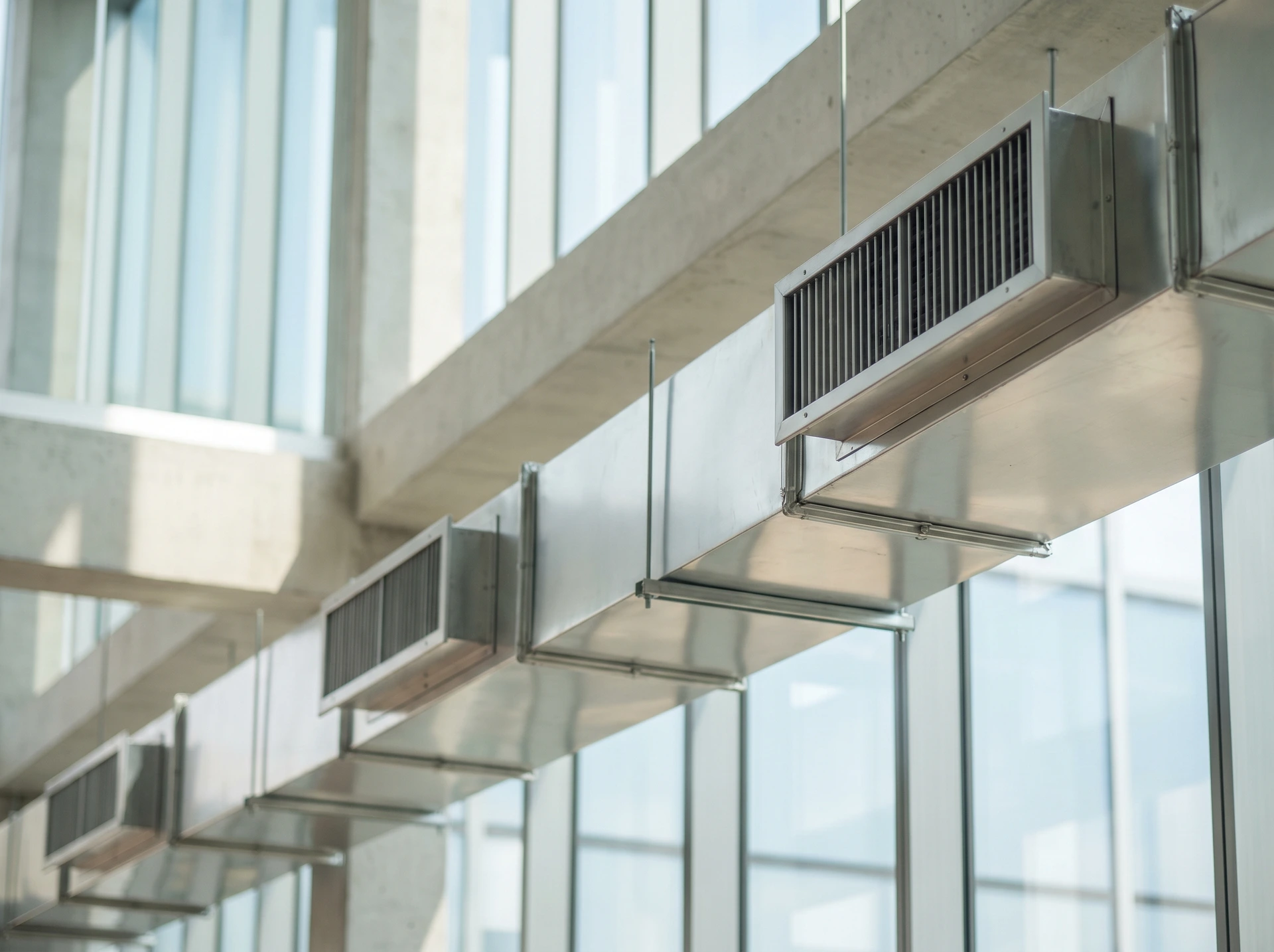 Ventilationskanaler i metall hänger från tak i modern glasbyggnad.